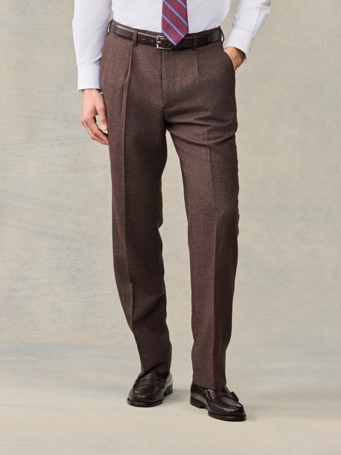 Cropped front view of a man in brown puppytooth trousers, white shirt, and pink striped tie.