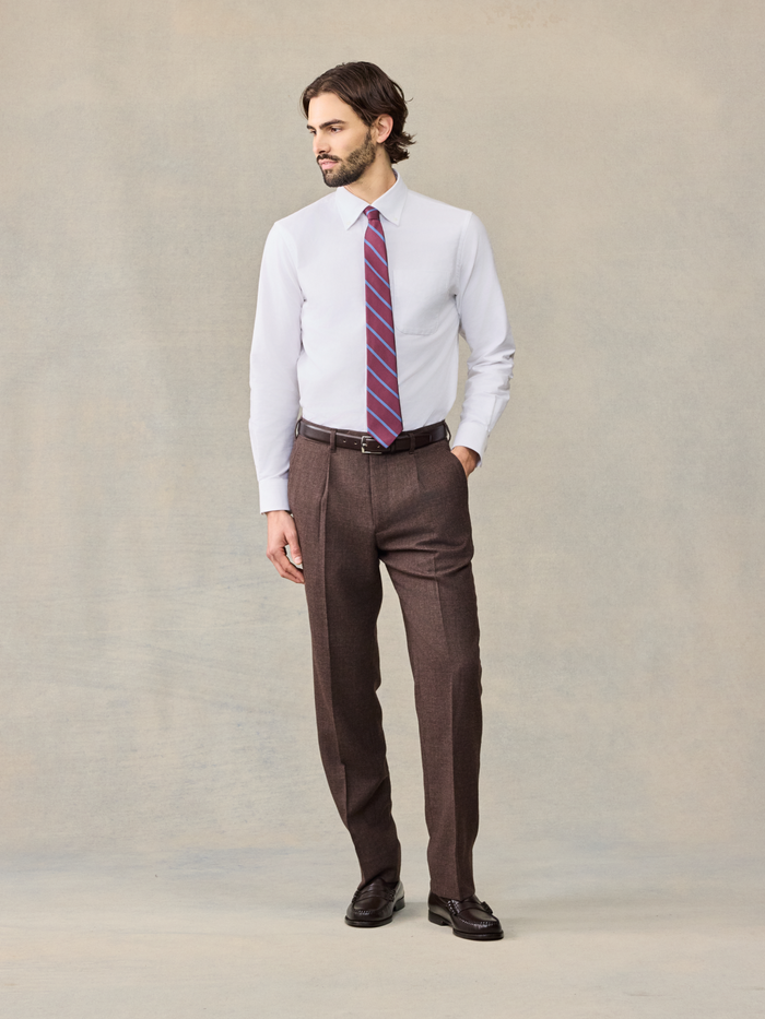 Man in a white shirt and pink striped tie wearing brown puppytooth trousers, full body front.