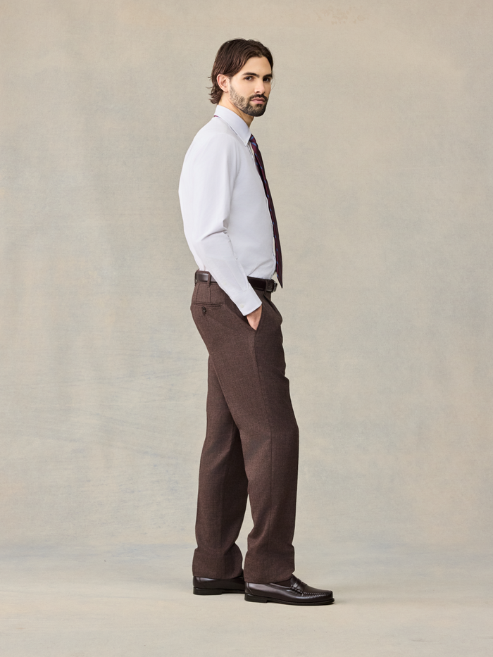 Side view of a man in a white shirt and brown puppytooth trousers, full body.