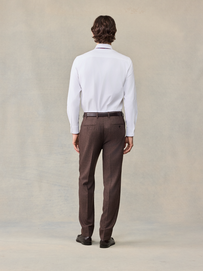 Back view of a man in a white shirt and brown puppytooth trousers, full body.
