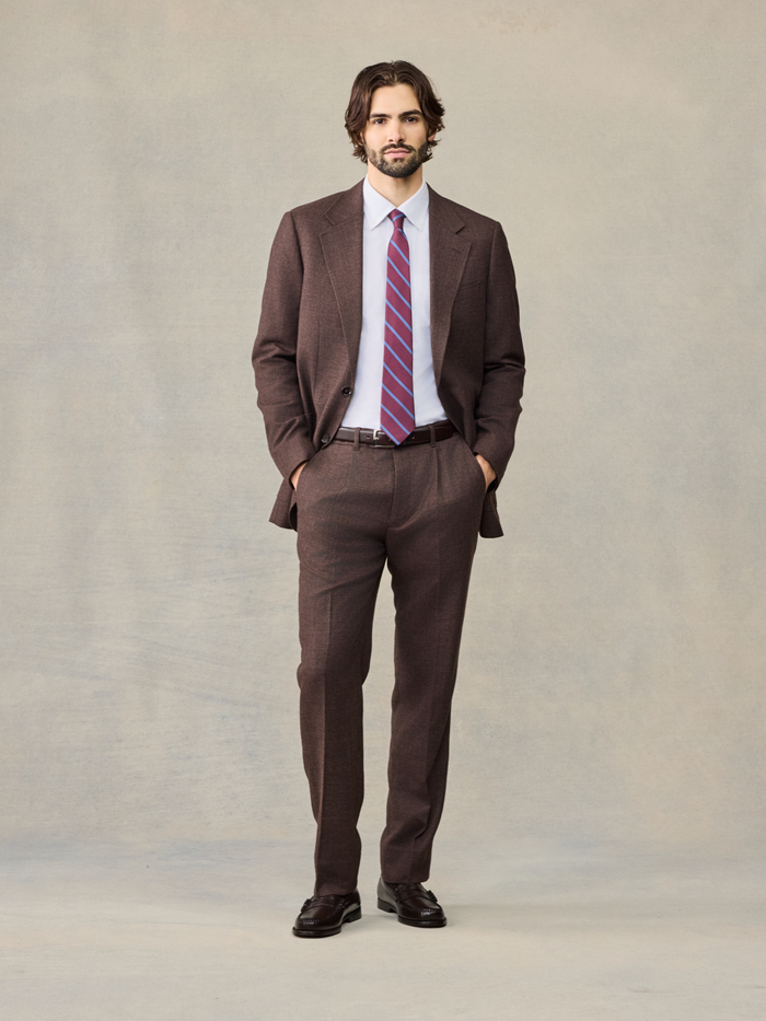Man in a full brown puppytooth suit with a pink striped tie, standing front view.