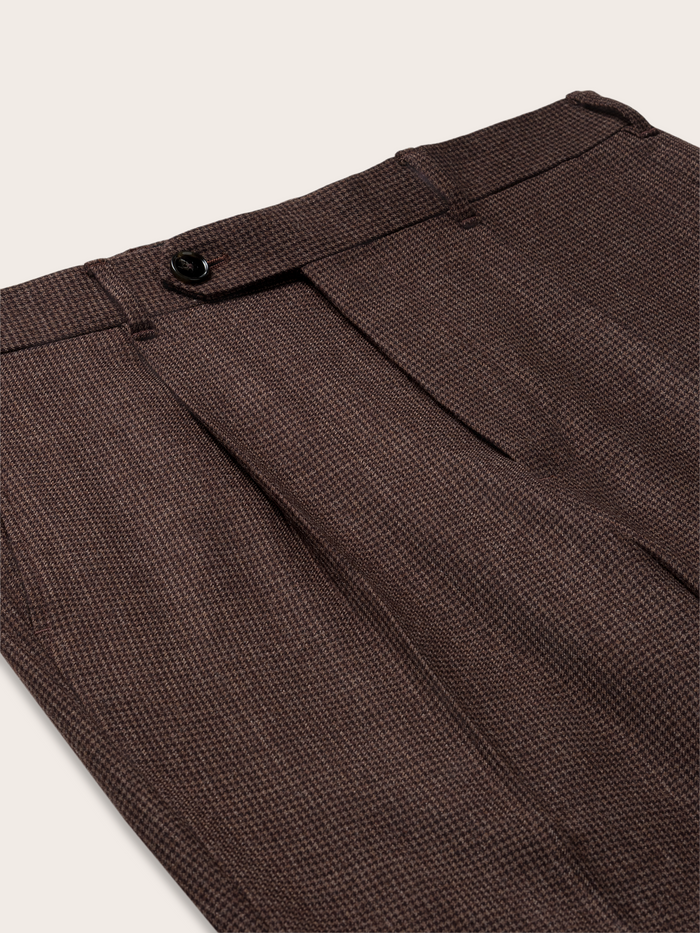Close-up of brown puppytooth trousers' pleated waistband and side pocket.