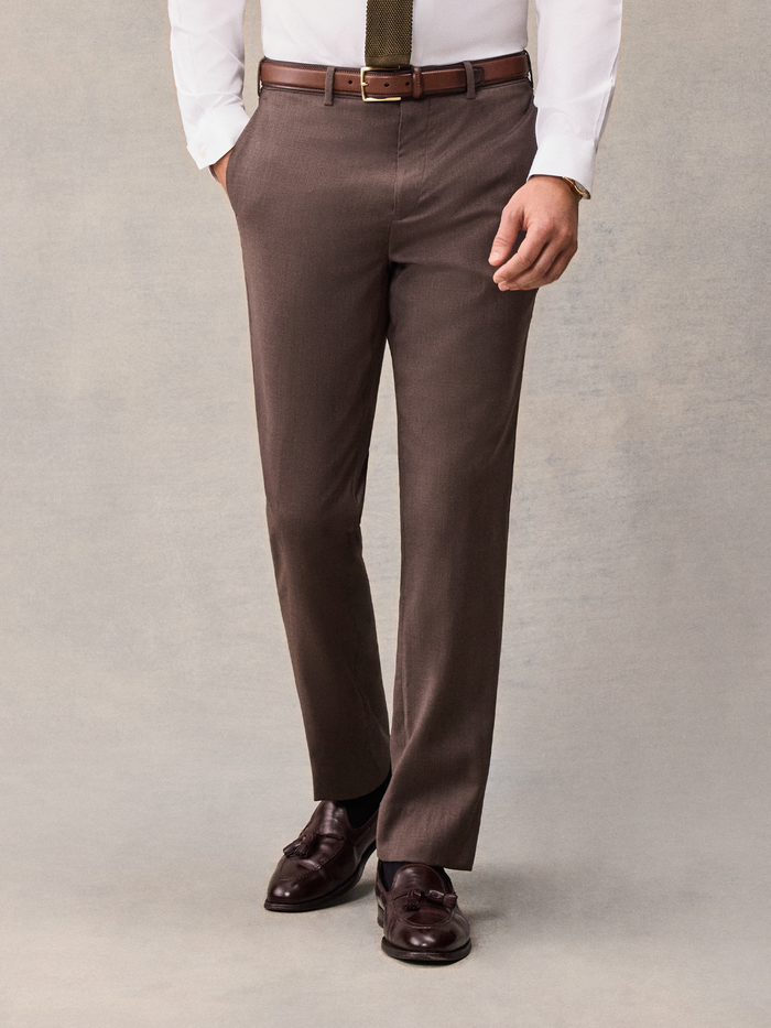 Cropped front view of a man in brown suit trousers with an olive tie and brown belt.