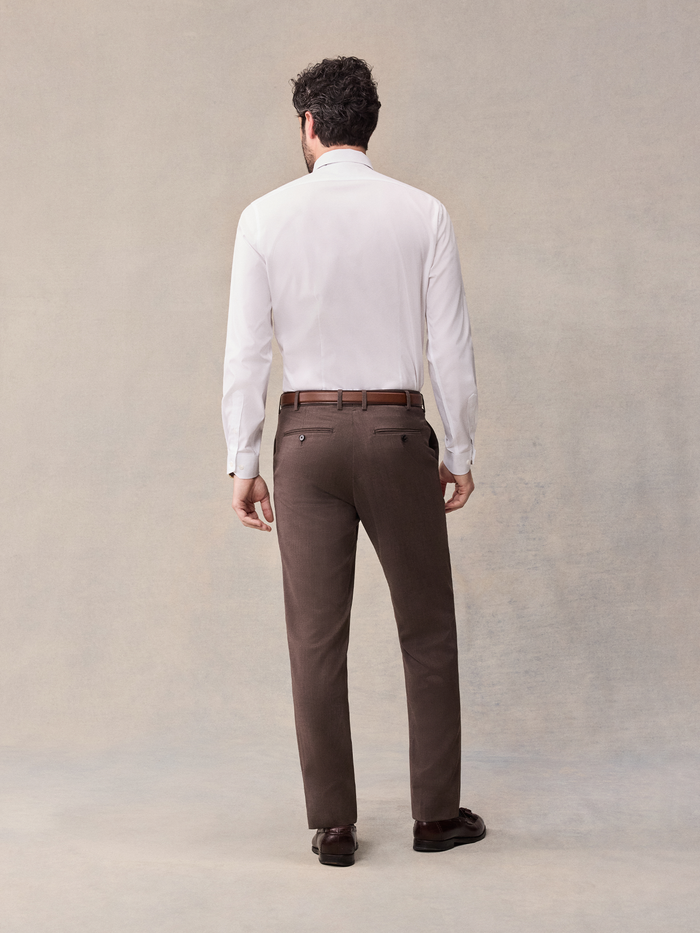 Back view of a man in a white shirt and brown suit trousers, full body.