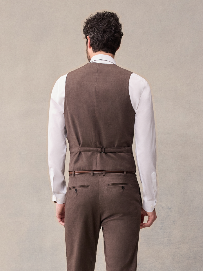 Back view of a man in a brown suit vest with a back strap, cropped view.