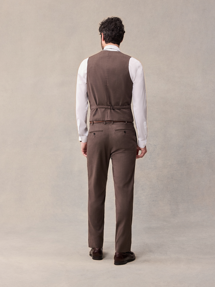 Back view of a man in a brown suit vest and trousers, full body.