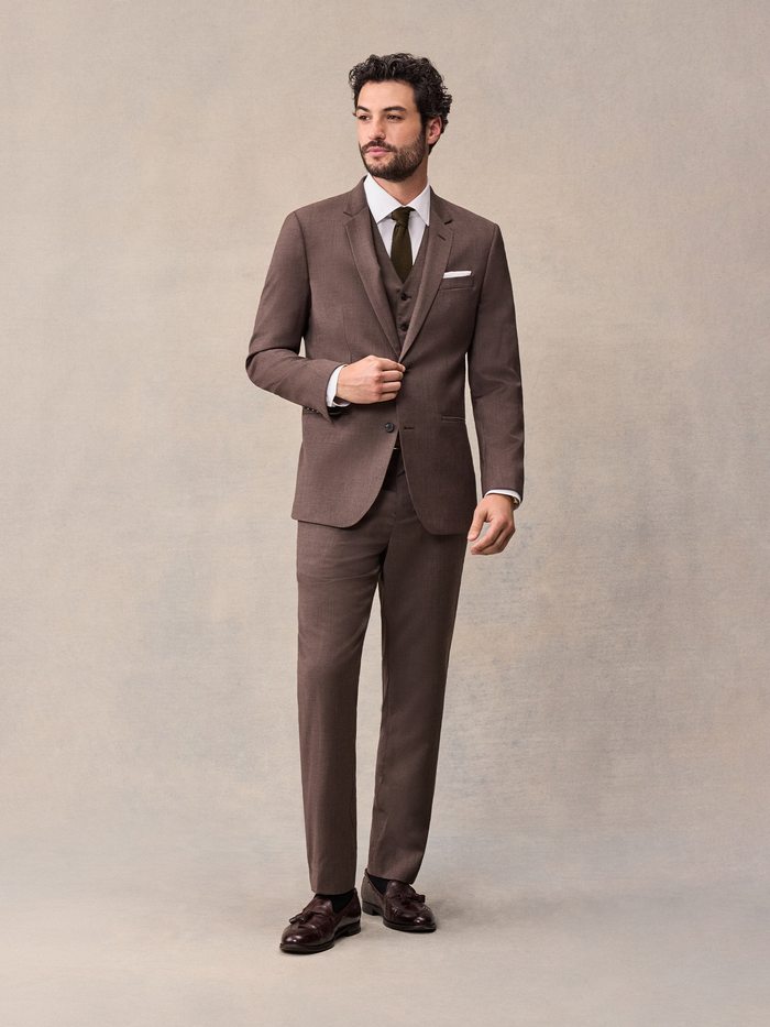 Man in a full brown three-piece suit with vest, jacket, and olive tie, buttoning the jacket.