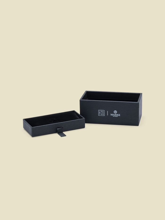 Two black textured gift boxes with brand labels, one open showing a fitted interior tray.