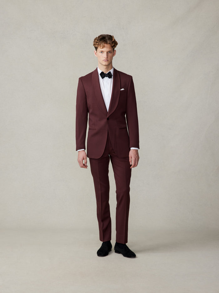 Man in a burgundy shawl-collar tuxedo with a black bow tie, full body front.