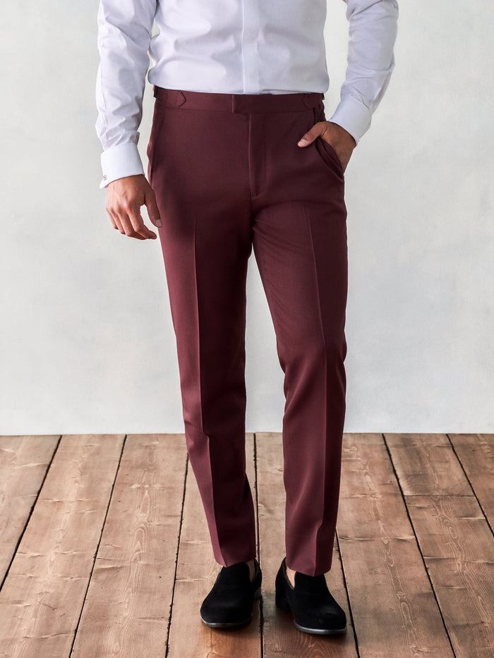 Cropped front view of a man in burgundy tuxedo trousers and a white shirt.