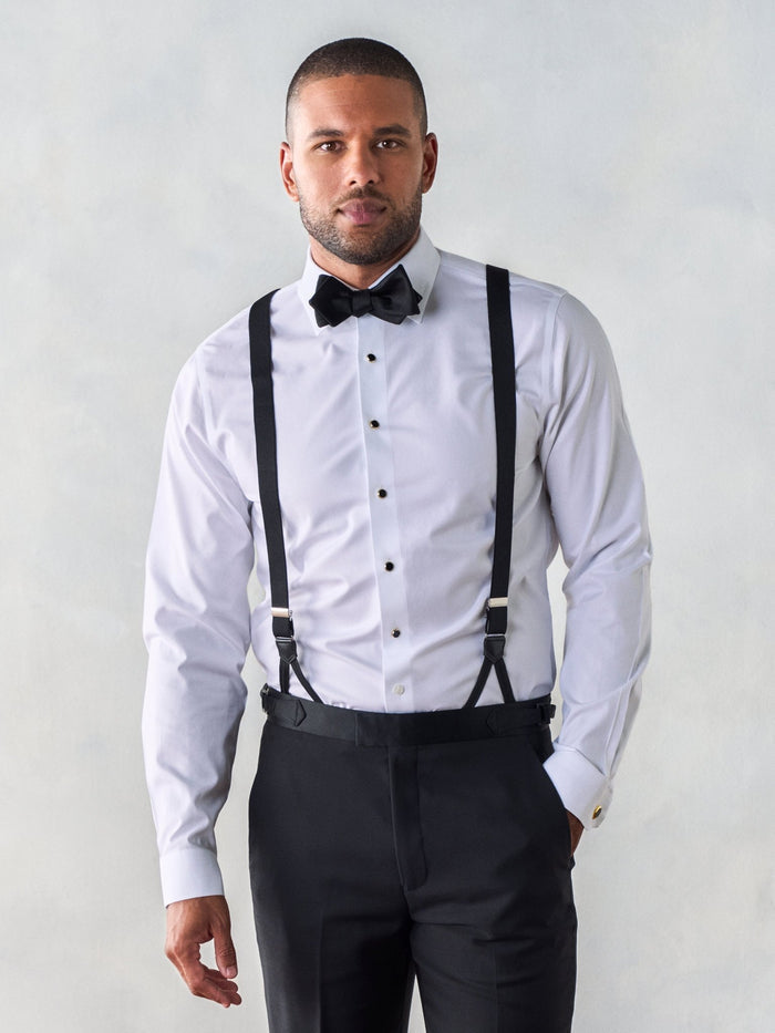 Man in a white tuxedo shirt with black button suspenders and a black bow tie, front view.