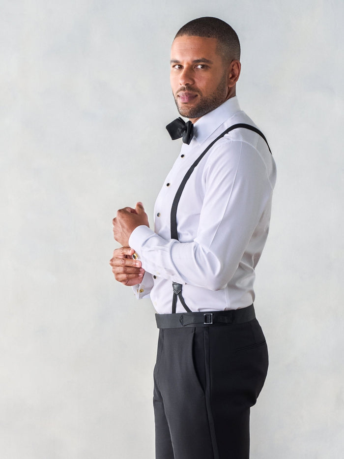 Side view of a man in a white tuxedo shirt with black button suspenders and bow tie.