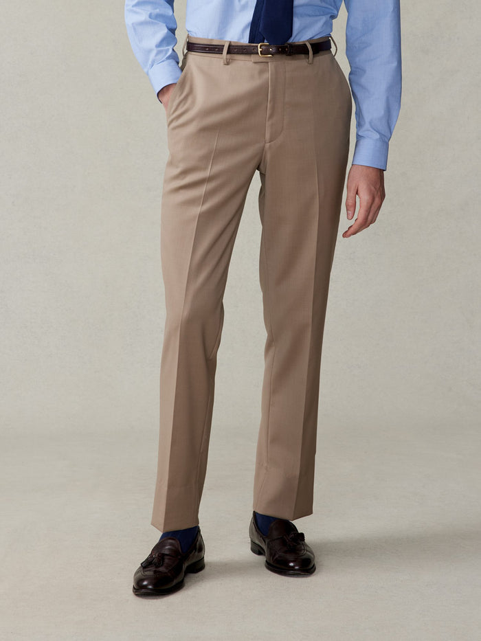 Cropped front view of a man in camel suit trousers, light blue shirt, and navy tie.