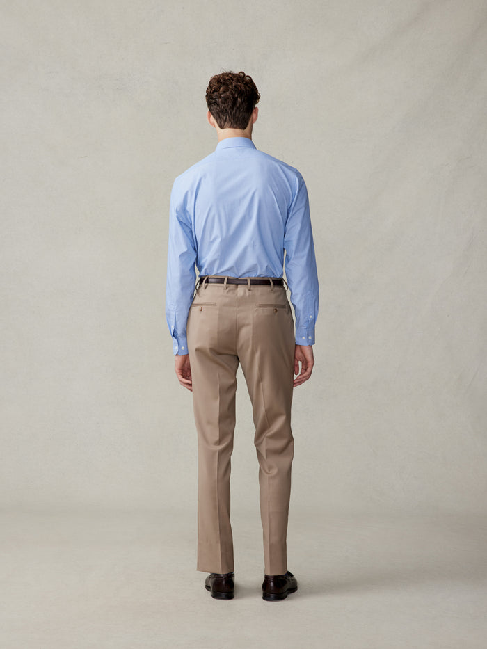 Back view of a man in a light blue shirt and camel suit trousers, full body.