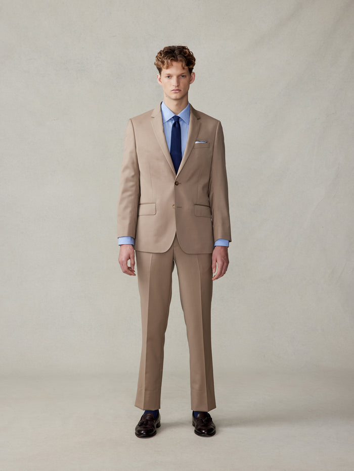 Man in a camel suit with a light blue shirt and navy tie, full body front.