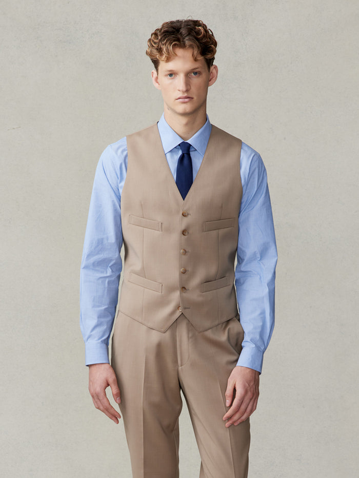 Man in a camel suit vest, light blue shirt, and navy tie, cropped front view.