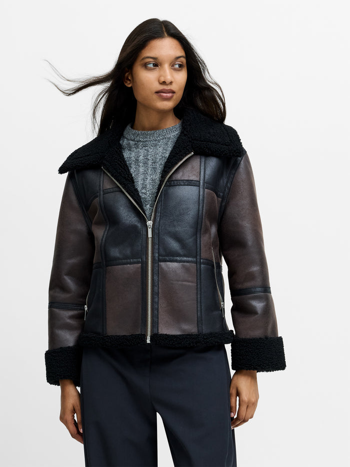 A woman wearing a brown faux suede aviator jacket with a faux shearling trim, zip through jacket, and side pockets.