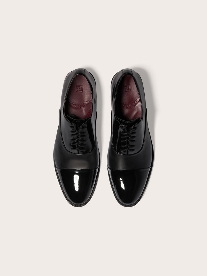 Pair of black cap-toe dress shoes in patent and calf leather, top-down view with burgundy insoles.