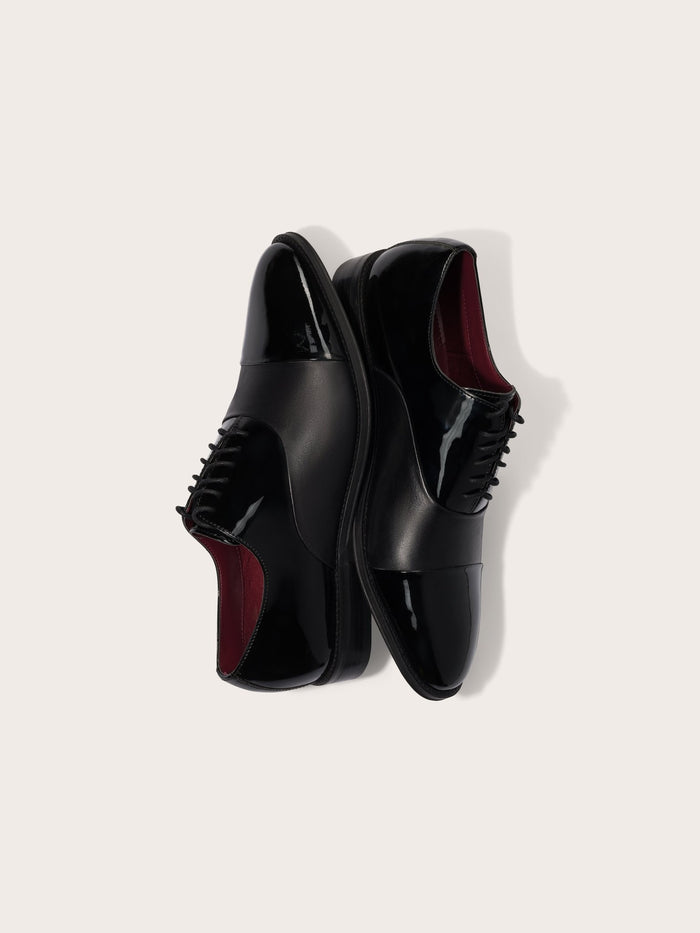 A pair of black dress shoes with a glossy finish and burgundy interior.