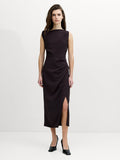 A woman wearing a sleeveless, draped midi mocha brown dress with a straight neckline and a side slit hem.