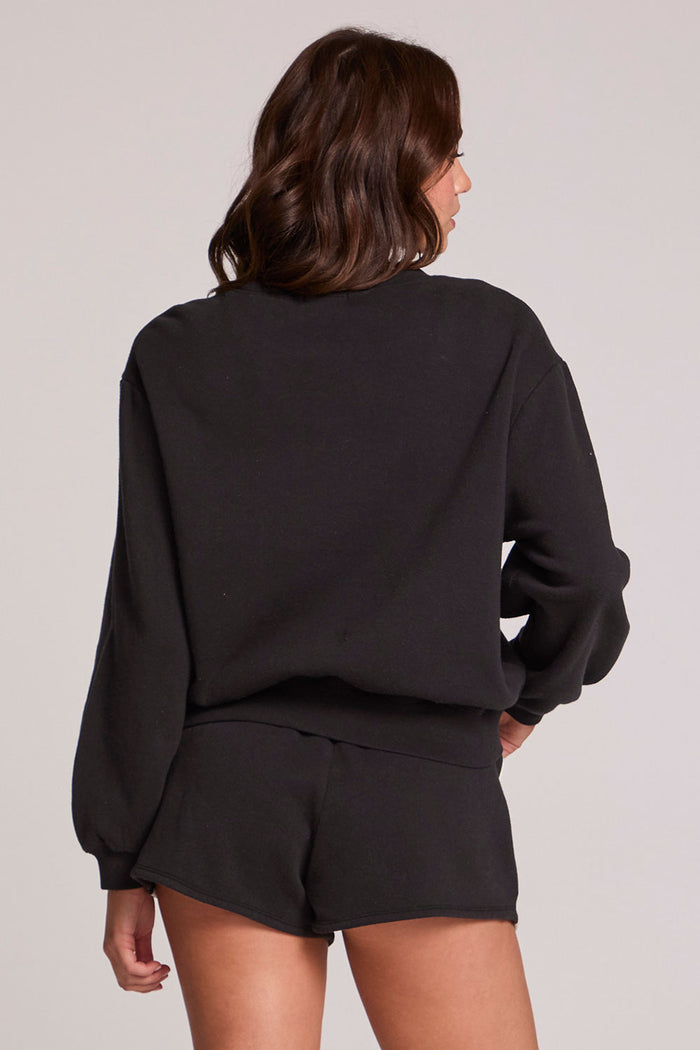 Back view of a woman wearing the Chaser  Cashbah Black Pullover on a neutral background with matching black shorts