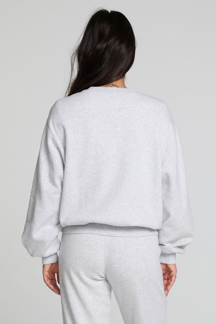 Back view of a woman wearing the Chaser  Cashbah Heather Grey Pullover and grey pants on a neutral background