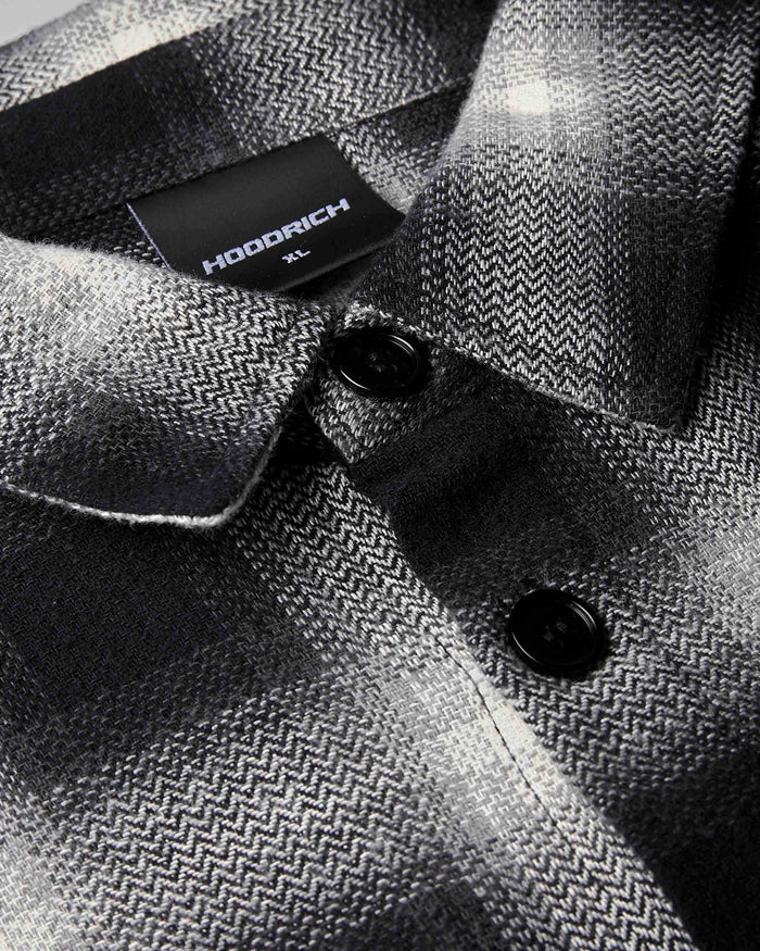 Close-up of a HODDRICH men's button-down shirt featuring a black and gray herringbone pattern, with a black brand label visible on the collar.