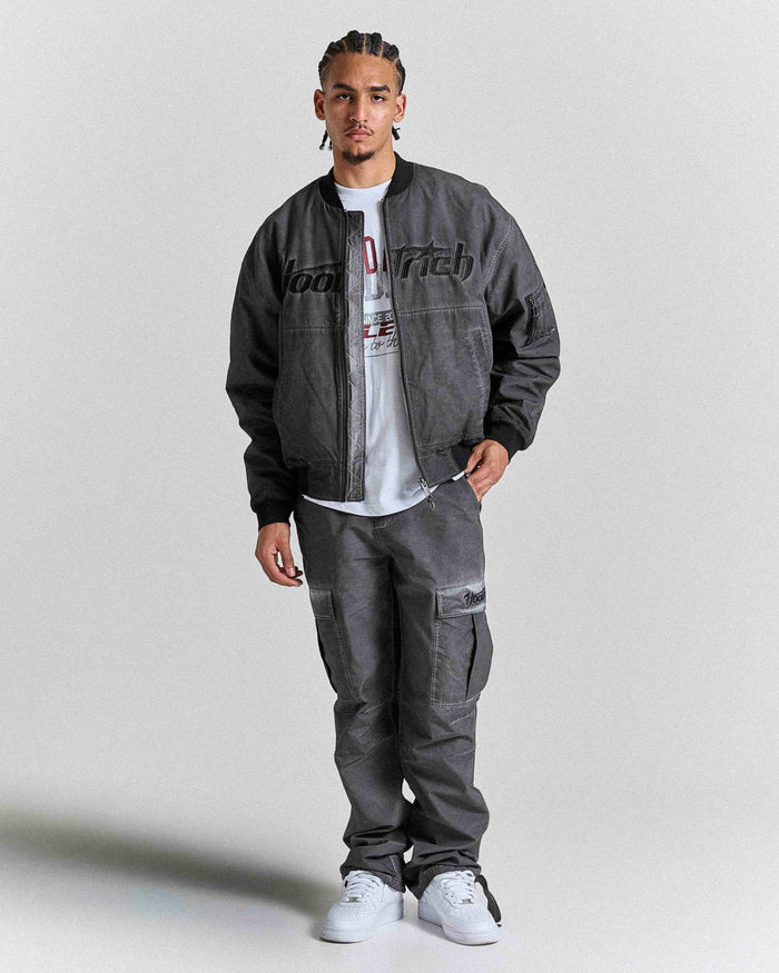 Person wearing a dark gray jacket and pants with a white shirt underneath on a light gray background