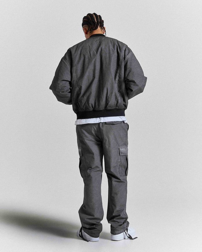 Person wearing a gray bomber jacket and pants on a plain background