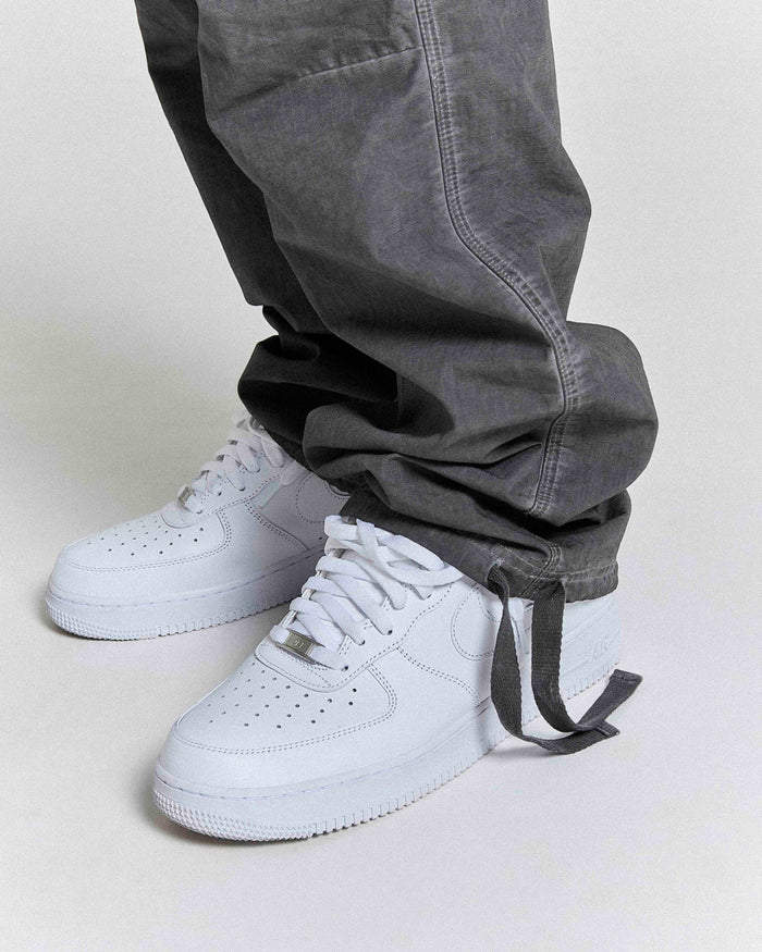 White sneakers with a gray pant cuff on a light gray background