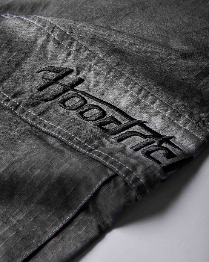 Close-up of dark gray denim fabric with a large embroidered black 'Hoodrich' logo patch on the pocket.