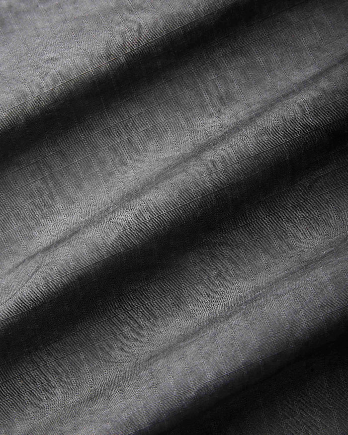 A close-up of dark gray textured fabric with a subtle woven grid pattern and soft diagonal folds.