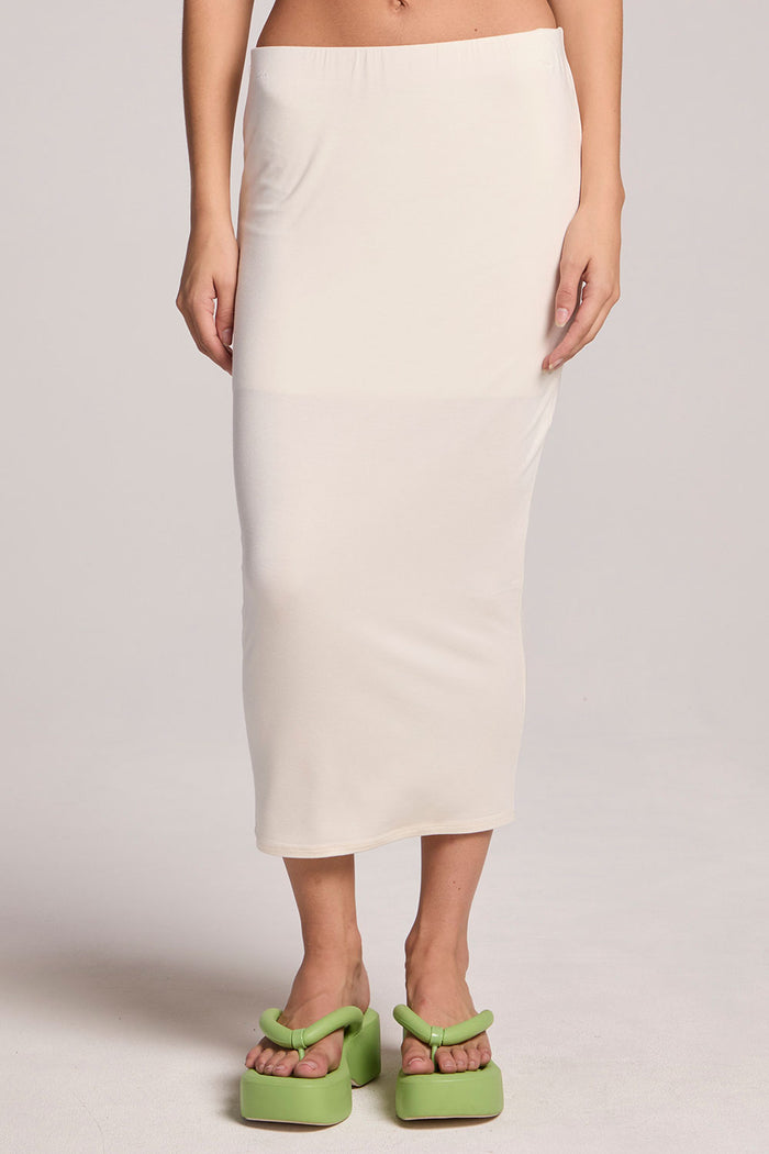 A front view of a woman wearing the Chaser Coconut Milk Catch Midi Skirt and slides on a neutral background