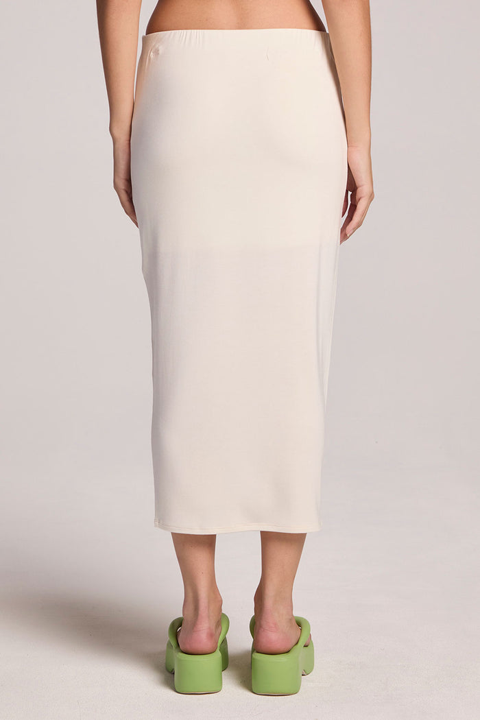 A back view of a woman wearing the Chaser Coconut Milk Catch Midi Skirt and green slides on a neutral background