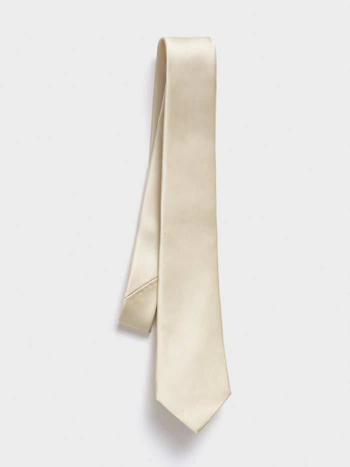 Champagne silk necktie with twill texture, draped diagonally on a grey background.