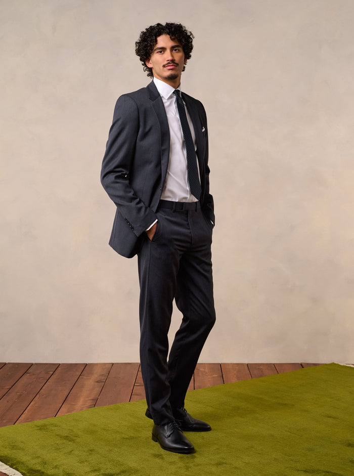 Man in a charcoal suit at a three-quarter angle, one hand in his pocket.