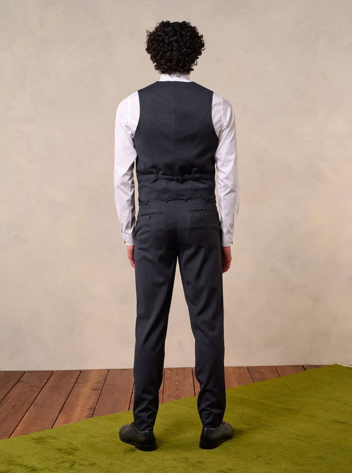 Back view of a man in a charcoal suit vest and trousers, full body.