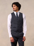 A man in a charcoal suit vest over a white shirt with a navy dotted tie