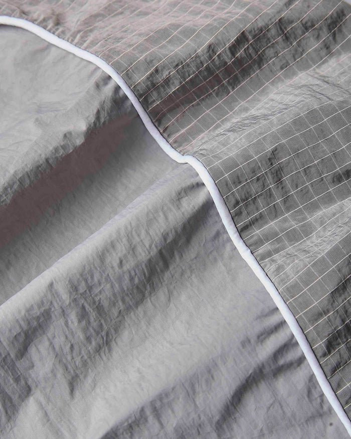 Close-up of a gray quilted fabric with a subtle grid pattern and a contrasting white piping border.