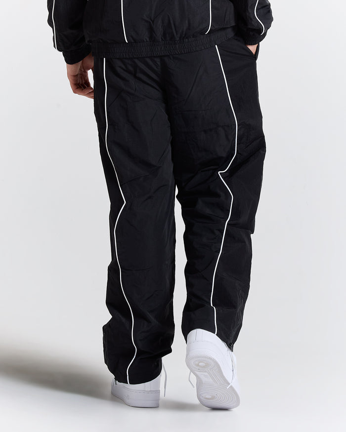 Black tracksuit with white piping worn by a person on a light gray background