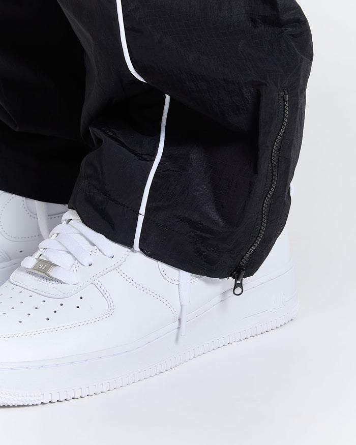 Close-up of a person wearing black pants with white piping and white sneakers on a white background