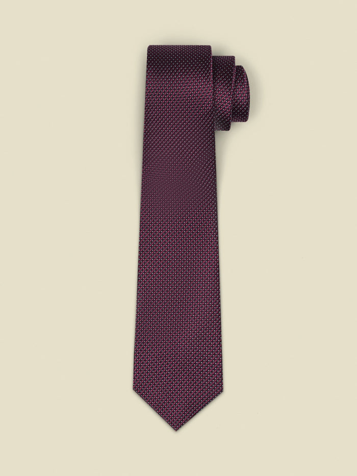 Chianti-red necktie with a fine dotted texture, rolled on a cream background.