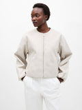A woman wearing an oatmeal, soft textured bomber jacket with a zip down fastening, long sleeves and 2 side pockets.