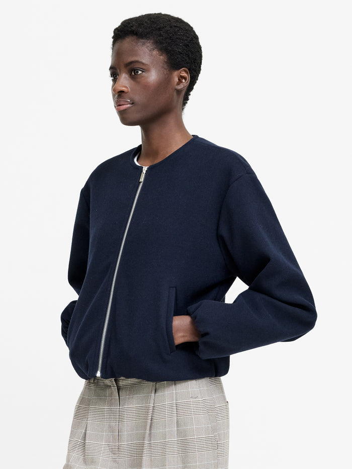 A woman wearing a navy bomber jacket with long sleeves, a sleek zip front and two side pockets.