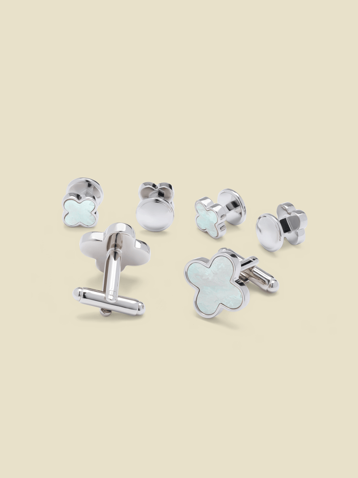Silver clover-shaped cufflinks and studs with mother-of-pearl inlay, on a cream background.