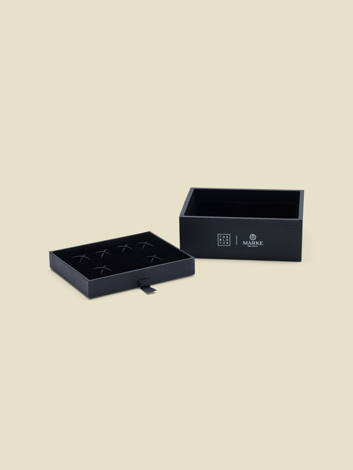 Two black textured boxes, one open with an X-slotted tray for cufflinks and studs.