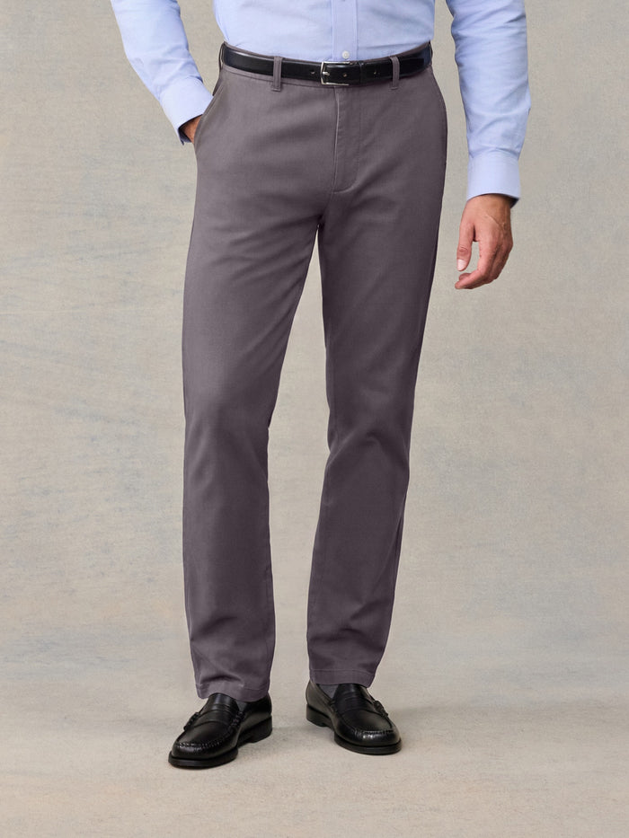 Man from waist down wearing grey chino pants with a black belt and black loafers.