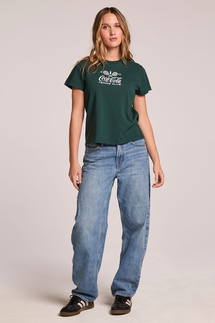 Full body front view of a woman wearing the Chaser   Coca Cola Tennis Club Tee  and sneakers on a neutral background