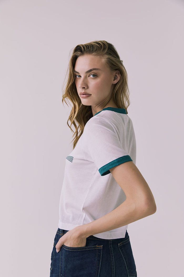 Back view of a woman wearing Chaser's white Coca Cola The Real Thing tee and blue jeans on a plain background