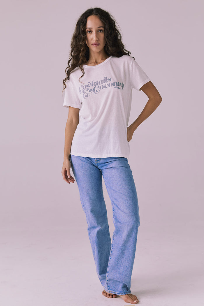 Model wearing the Chaser Cocktails & Coconuts Tee styled with light wash denim for a laid-back everyday look